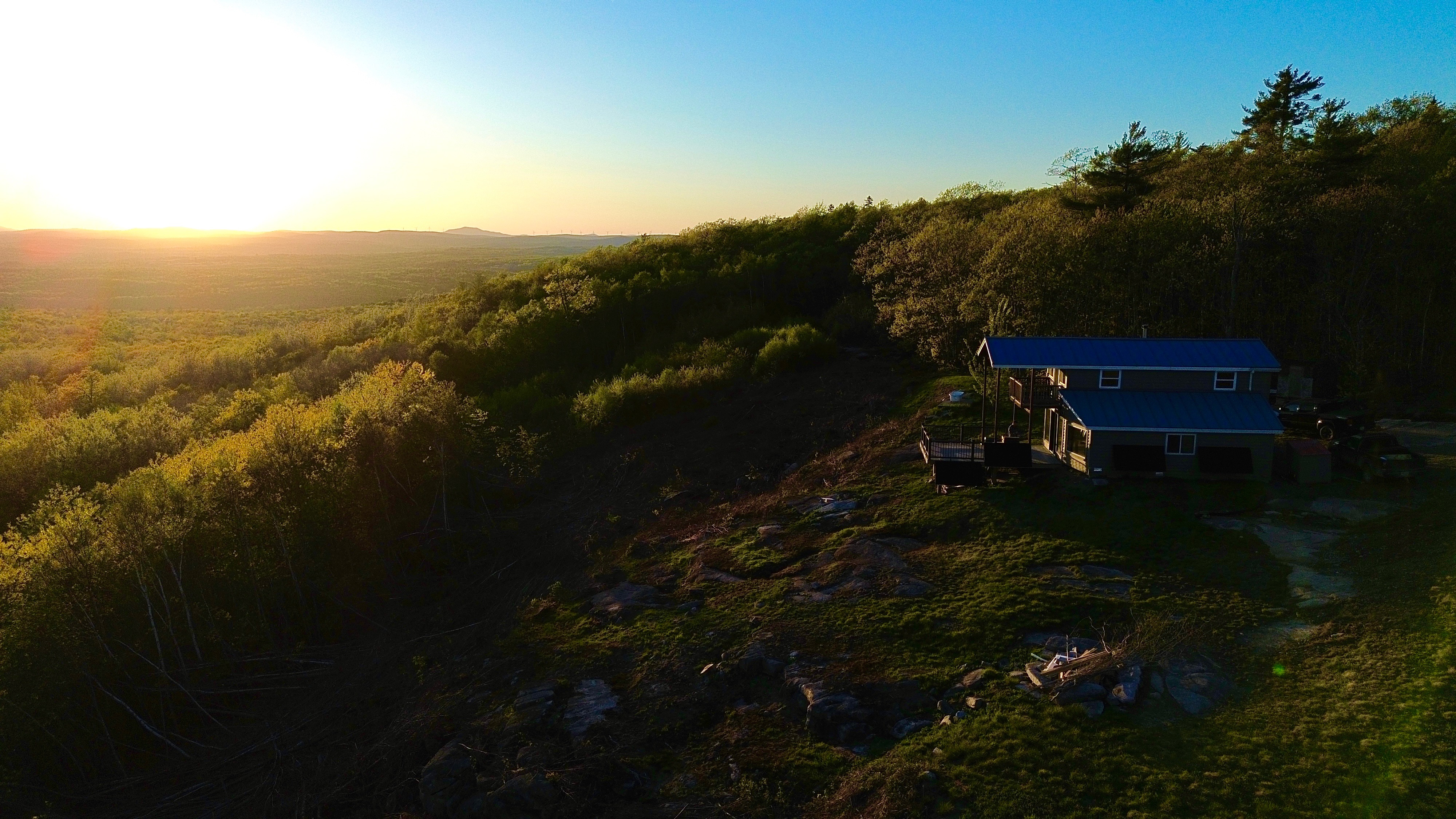 Golden-hour drone view of the home along the ridge, sunset over the western Maine hills